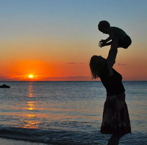 mom lifting a baby by the sea on the backdrop of a sunset